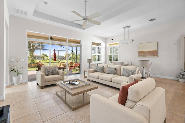 tiled living room with a tray ceiling and ceiling fan