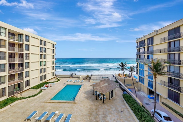 view of pool featuring a water view, a patio, and a beach view