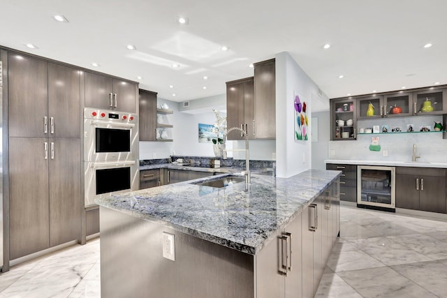 kitchen featuring a large island, sink, beverage cooler, double oven, and dark stone counters