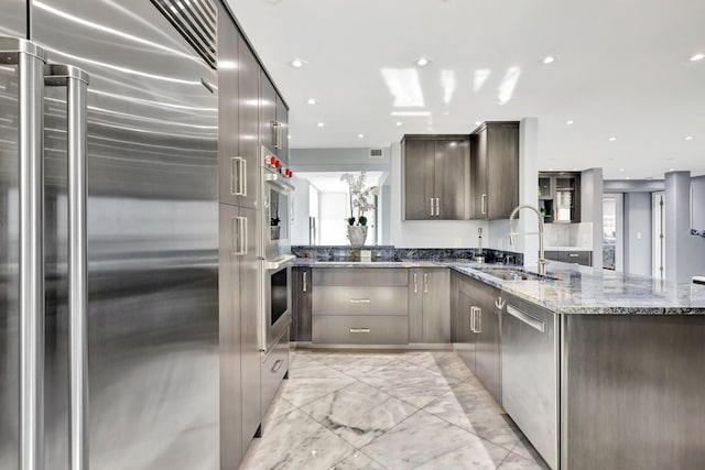 kitchen with kitchen peninsula, dark brown cabinetry, stainless steel appliances, sink, and dark stone countertops