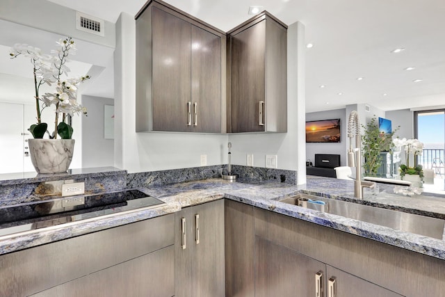 kitchen featuring dark brown cabinetry, black electric cooktop, sink, and dark stone counters