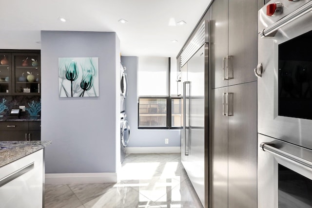 kitchen with stainless steel double oven, stacked washing maching and dryer, and stone counters