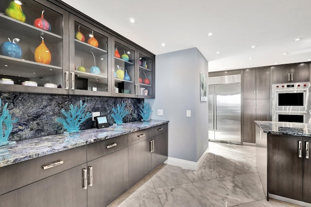 kitchen featuring backsplash, stainless steel appliances, light stone counters, and dark brown cabinetry