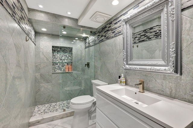 bathroom featuring a tile shower, vanity, tile walls, and toilet