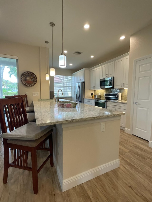 kitchen featuring white cabinets, decorative light fixtures, appliances with stainless steel finishes, and light hardwood / wood-style flooring