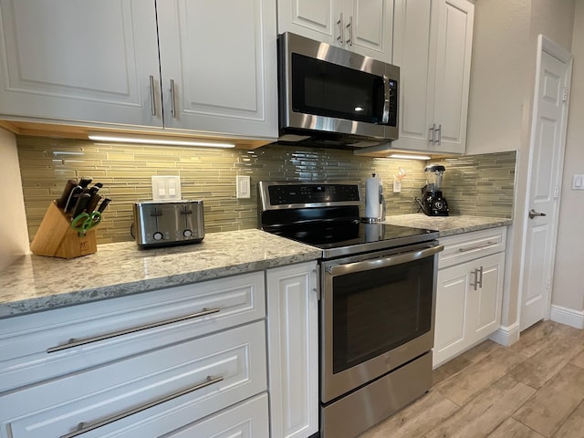 kitchen featuring backsplash, white cabinets, light wood-type flooring, light stone counters, and stainless steel appliances