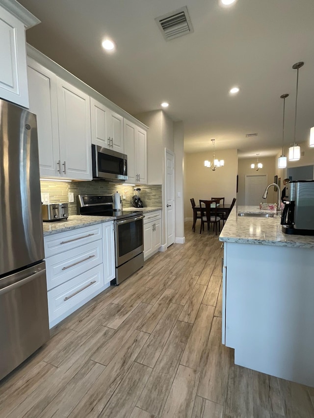 kitchen featuring sink, light wood-type flooring, decorative light fixtures, white cabinetry, and stainless steel appliances