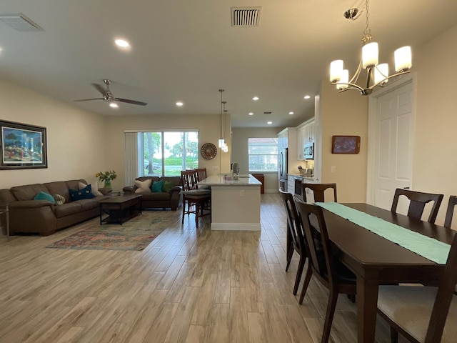 dining room featuring ceiling fan with notable chandelier and light hardwood / wood-style flooring