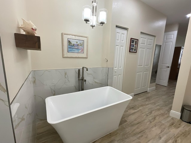 bathroom featuring a tub to relax in, an inviting chandelier, hardwood / wood-style flooring, and tile walls