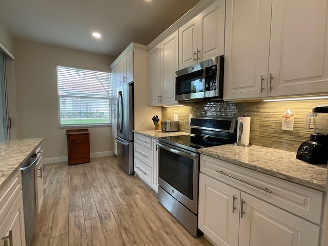 kitchen with white cabinetry, stainless steel appliances, tasteful backsplash, light stone counters, and light hardwood / wood-style flooring