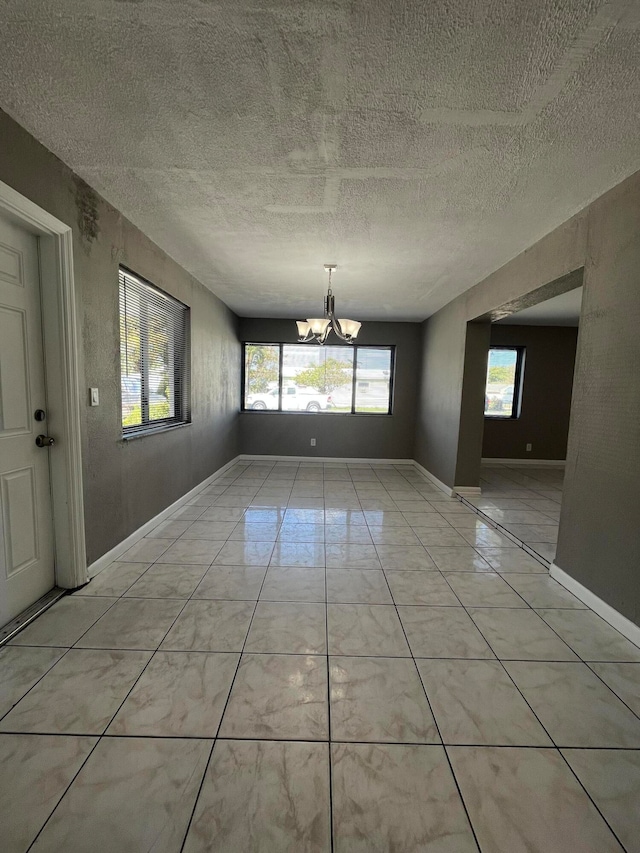 tiled empty room featuring a textured ceiling, an inviting chandelier, and a healthy amount of sunlight