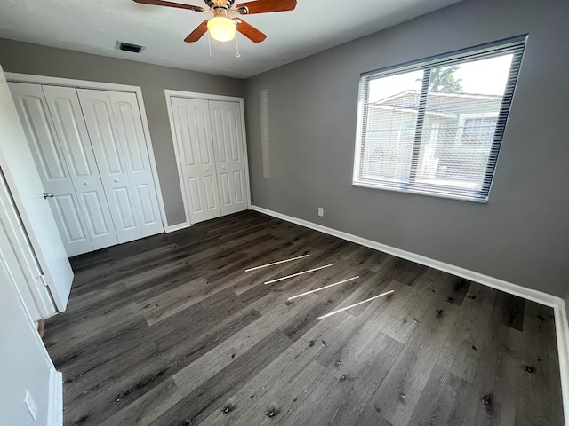 unfurnished bedroom with multiple closets, ceiling fan, and dark wood-type flooring