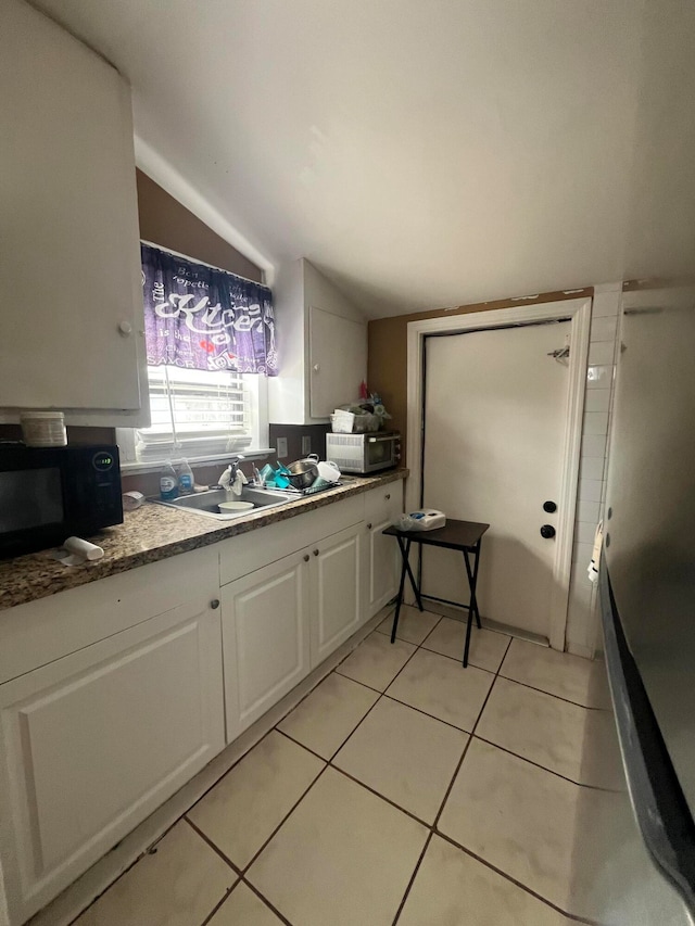 kitchen with white cabinetry, sink, light tile patterned floors, and lofted ceiling