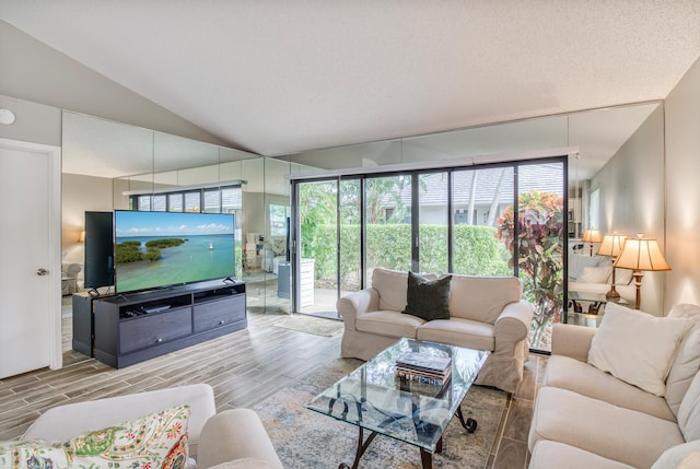 living room featuring a textured ceiling, light wood-type flooring, and vaulted ceiling