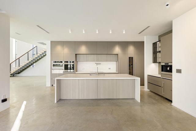 kitchen with gray cabinetry, stainless steel oven, a spacious island, and sink