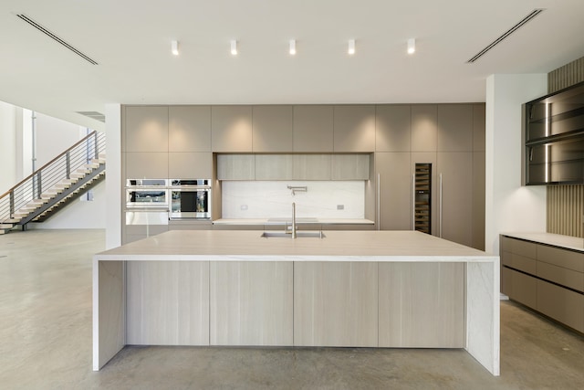 kitchen with light brown cabinets, sink, a spacious island, and stainless steel oven