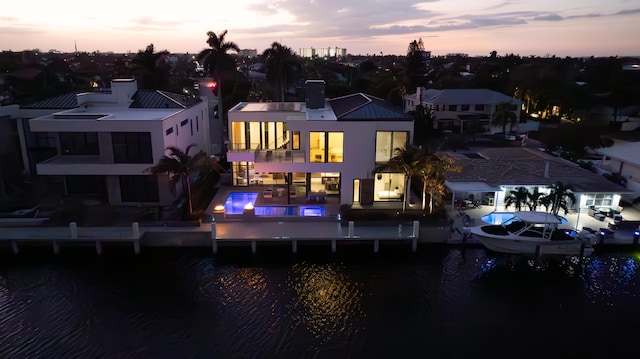 back house at dusk featuring a balcony and a water view