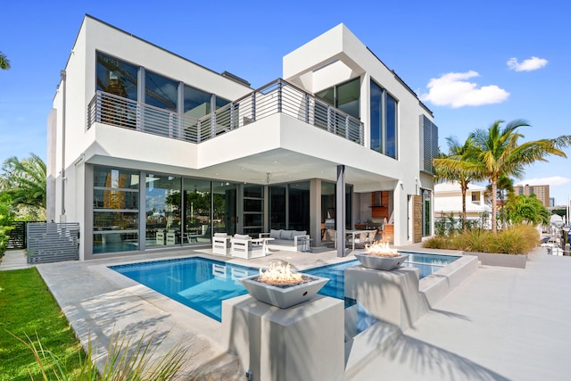 rear view of house with a balcony, an outdoor living space with a fire pit, and a patio