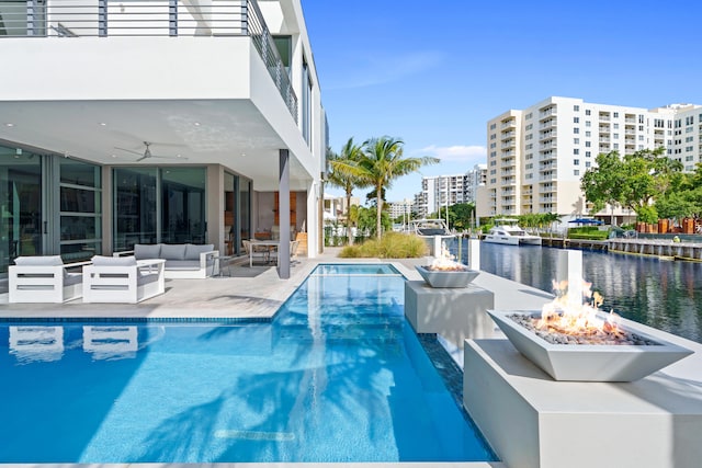 view of pool featuring ceiling fan, a water view, an outdoor living space with a fire pit, and a patio