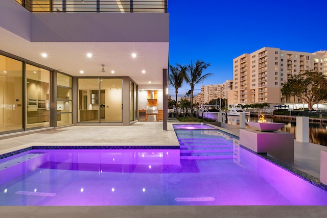 pool at dusk featuring a jacuzzi, a patio, and a water view