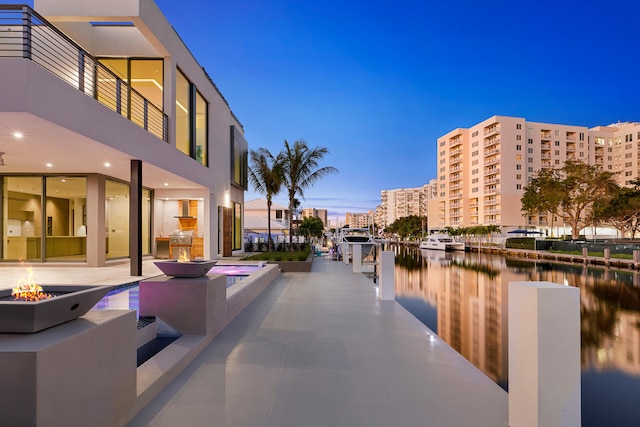 patio terrace at dusk with a water view, a jacuzzi, and grilling area