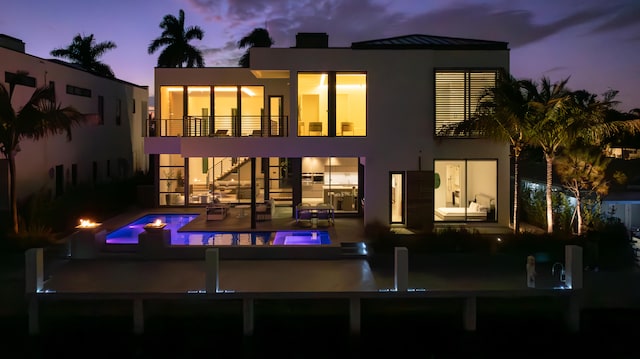 back house at dusk with a swimming pool with hot tub, a patio, and a balcony