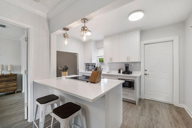 kitchen with appliances with stainless steel finishes, white cabinetry, hanging light fixtures, light hardwood / wood-style floors, and a kitchen bar