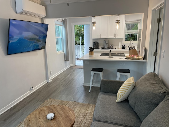 kitchen featuring an AC wall unit, a breakfast bar, white cabinetry, hanging light fixtures, and hardwood / wood-style flooring