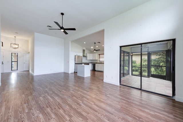 unfurnished living room featuring a wealth of natural light, high vaulted ceiling, light hardwood / wood-style floors, and ceiling fan with notable chandelier