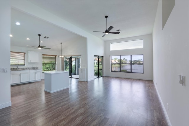 unfurnished living room featuring a wealth of natural light, a towering ceiling, dark hardwood / wood-style floors, and ceiling fan