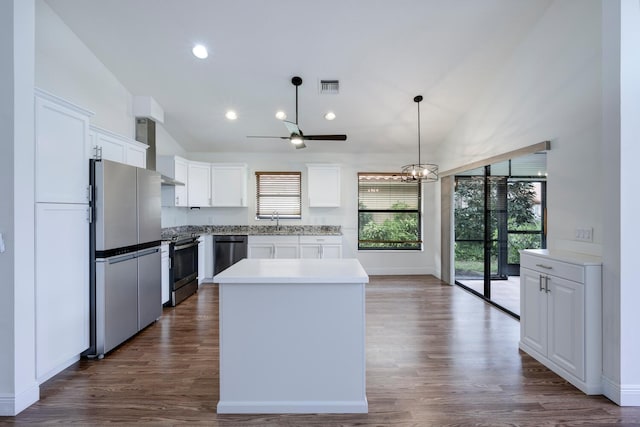 kitchen featuring appliances with stainless steel finishes, dark wood-type flooring, wall chimney range hood, white cabinets, and a center island