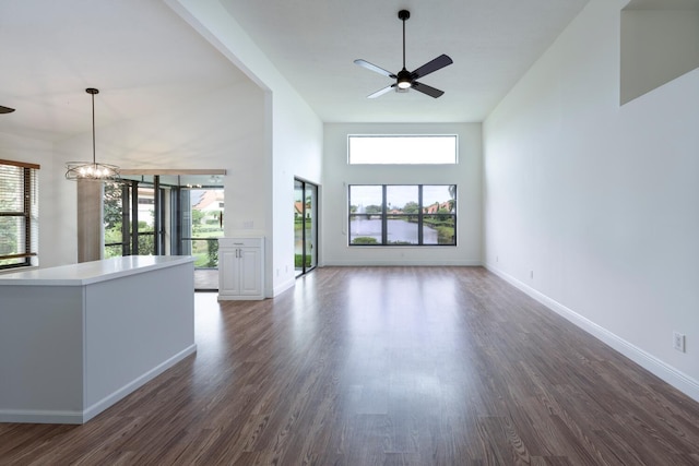 unfurnished living room with ceiling fan with notable chandelier, a healthy amount of sunlight, dark hardwood / wood-style flooring, and a towering ceiling