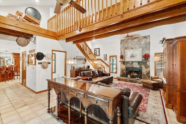 tiled living room with ceiling fan, beam ceiling, a stone fireplace, and a high ceiling