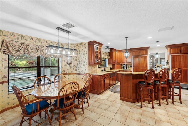 kitchen with a textured ceiling, light stone counters, a center island, and decorative light fixtures