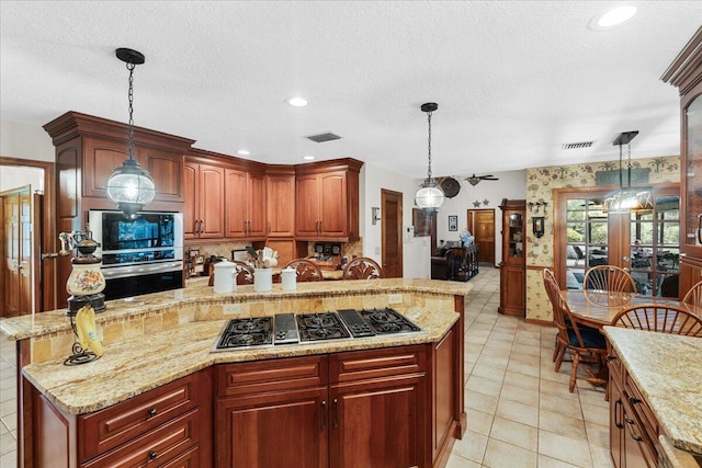 kitchen featuring hanging light fixtures, light stone countertops, a textured ceiling, appliances with stainless steel finishes, and a kitchen island