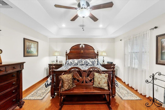 bedroom featuring a tray ceiling, ceiling fan, and light wood-type flooring