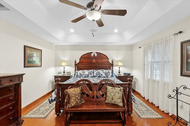 bedroom featuring a raised ceiling, ceiling fan, and light hardwood / wood-style flooring