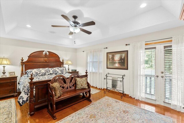 bedroom featuring ceiling fan, access to exterior, a tray ceiling, and light hardwood / wood-style flooring