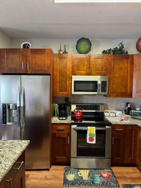 kitchen with light stone countertops, a textured ceiling, stainless steel appliances, and light hardwood / wood-style flooring