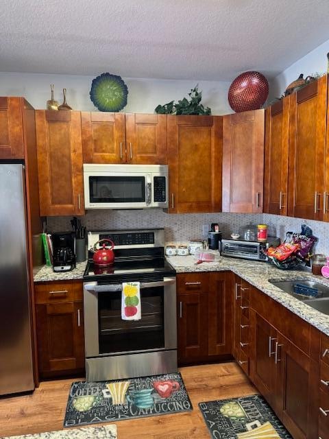 kitchen featuring sink, a textured ceiling, appliances with stainless steel finishes, light hardwood / wood-style floors, and light stone counters