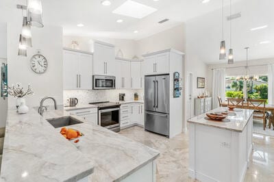 kitchen with sink, light stone countertops, appliances with stainless steel finishes, decorative light fixtures, and white cabinetry