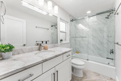 full bathroom with vanity, enclosed tub / shower combo, and toilet