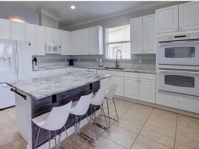 kitchen with a center island, sink, light stone counters, white appliances, and a kitchen bar