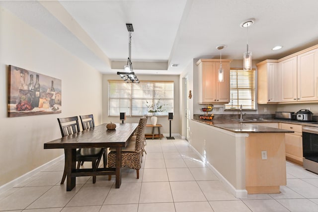 kitchen with sink, hanging light fixtures, a raised ceiling, light brown cabinetry, and light tile patterned floors