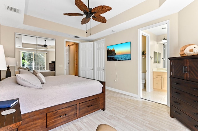 bedroom featuring ceiling fan, a raised ceiling, a barn door, light hardwood / wood-style flooring, and ensuite bathroom