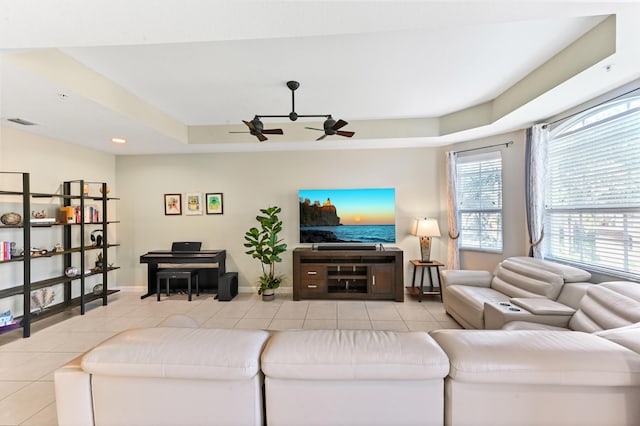 living room featuring a raised ceiling, ceiling fan, and light tile patterned floors