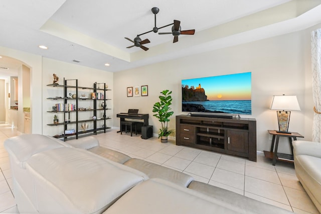 living room with ceiling fan, a raised ceiling, and light tile patterned floors