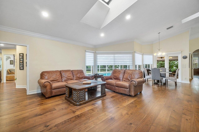 living room featuring hardwood / wood-style floors, a notable chandelier, ornamental molding, and lofted ceiling with skylight