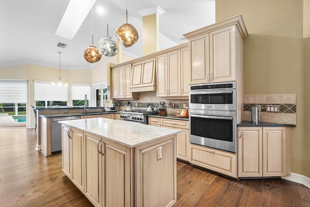 kitchen with a center island, hanging light fixtures, dark wood-type flooring, dark stone countertops, and appliances with stainless steel finishes