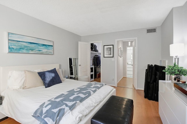 bedroom featuring a walk in closet, ensuite bath, a textured ceiling, light hardwood / wood-style floors, and a closet